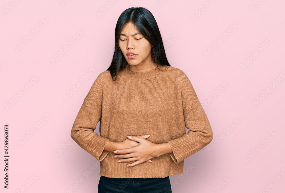 Beautiful young asian woman wearing casual winter sweater with hand on stomach because indigestion, painful illness feeling unwell. ache concept. Beautiful young asian woman wearing casual winter sweater with hand on stomach because indigestion, painful illness feeling unwell. ache concept.