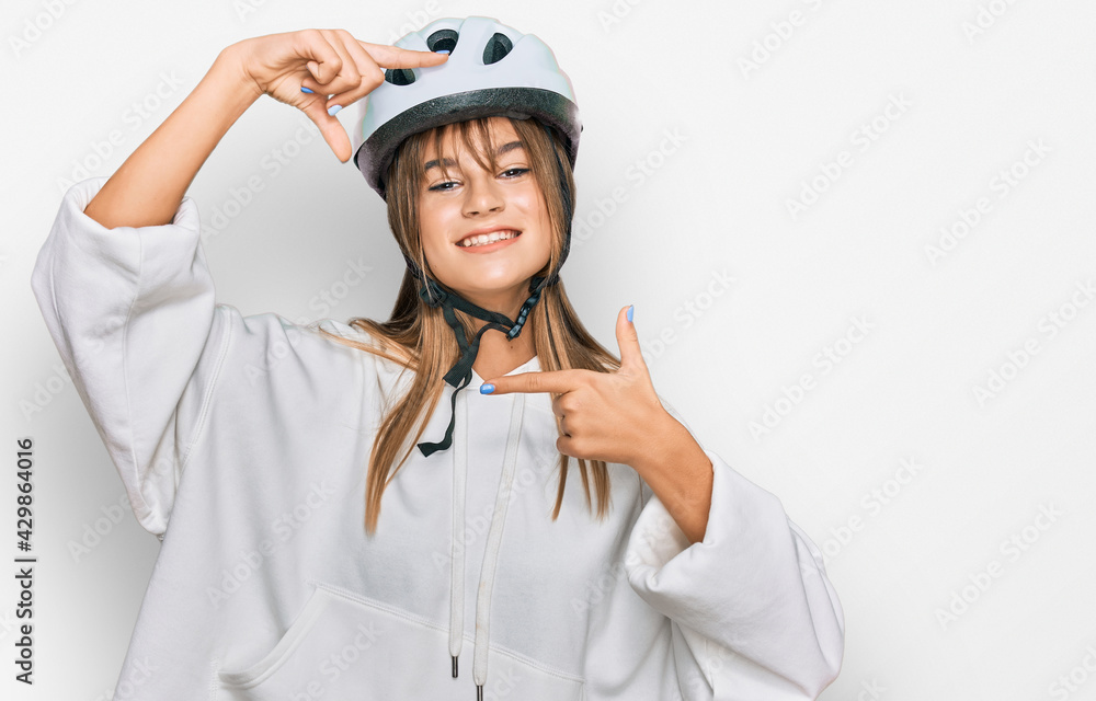 Teenager caucasian girl wearing bike helmet smiling making frame with hands and fingers with happy face. creativity and photography concept. Teenager caucasian girl wearing bike helmet smiling making frame with hands and fingers with happy face. creativity and photography concept.