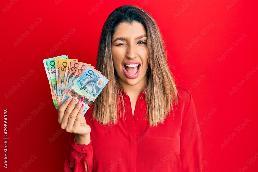 Beautiful brunette woman holding australian dollars winking looking at the camera with sexy expression, cheerful and happy face. Beautiful brunette woman holding australian dollars winking looking at the camera with sexy expression, cheerful and happy face.