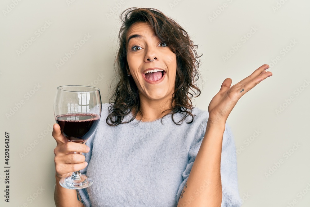 Young hispanic woman drinking a glass of red wine celebrating victory with happy smile and winner expression with raised hands Young hispanic woman drinking a glass of red wine celebrating victory with happy smile and winner expression with raised hands
