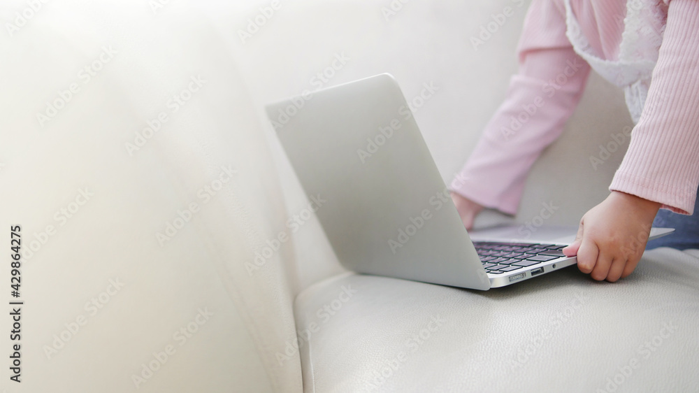 Naklejka premium Child hands put laptop computer on sofa using computer at home. Online remote learning, distance education, homeschooling, and online modern technology applications concepts.