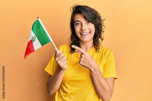 Young hispanic woman holding mexico flag smiling happy pointing with hand and finger