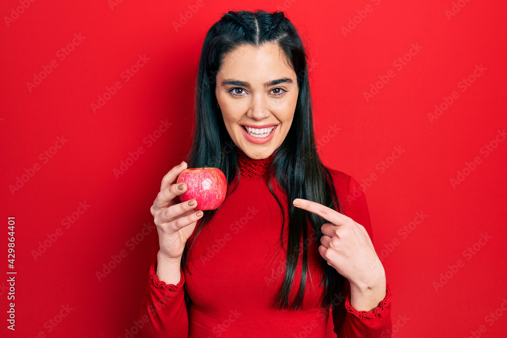 Young hispanic girl holding red apple smiling happy pointing with hand and finger Young hispanic girl holding red apple smiling happy pointing with hand and finger