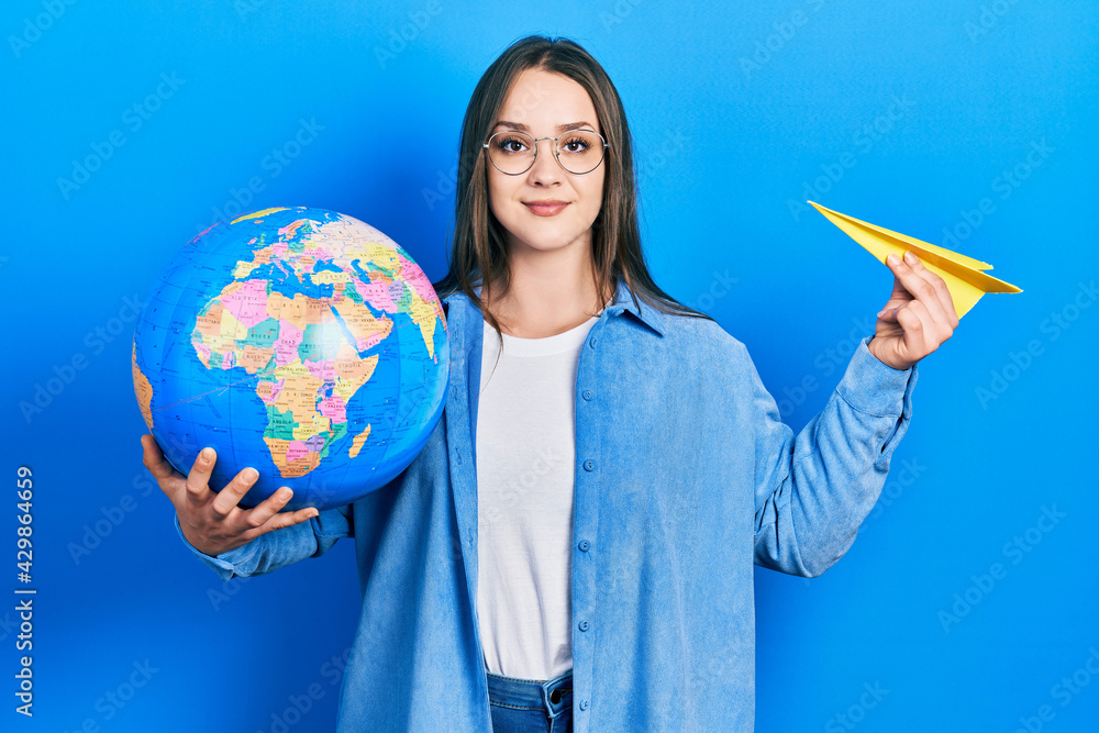 Fototapeta premium Young hispanic girl holding paper plane and world ball smiling with a happy and cool smile on face. showing teeth.