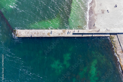 Sandy beach, concrete pier, clear sea water. Helicopter view.