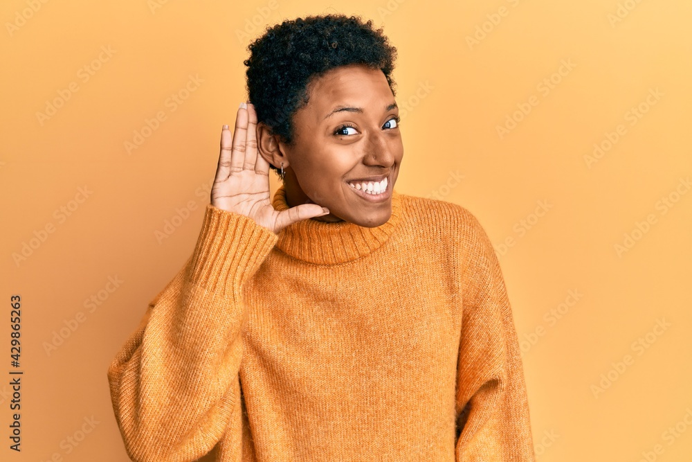 Young african american girl wearing casual clothes smiling with hand over ear listening an hearing to rumor or gossip. deafness concept. Young african american girl wearing casual clothes smiling with hand over ear listening an hearing to rumor or gossip. deafness concept.