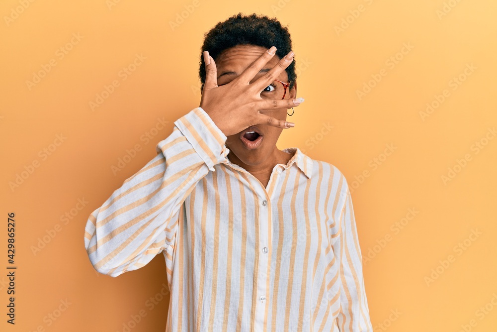 Young african american girl wearing casual clothes and glasses peeking in shock covering face and eyes with hand, looking through fingers afraid
