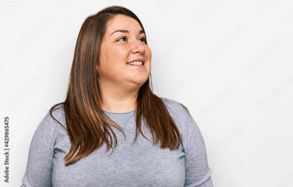Beautiful brunette plus size woman wearing casual clothes looking away to side with smile on face, natural expression. laughing confident.