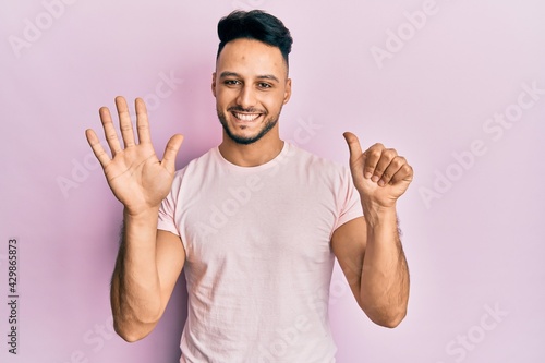 Young arab man wearing casual clothes showing and pointing up with fingers number six while smiling confident and happy.