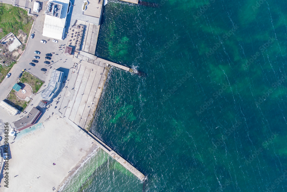 Sandy beach, concrete pier, clear sea water. Helicopter view.