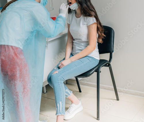 Doctor in protective workwear taking nose swab test from young woman. Close-up of woman having PCR or PLR testing at the hospital. Woman being screened for coronavirus in a laboratory. photo