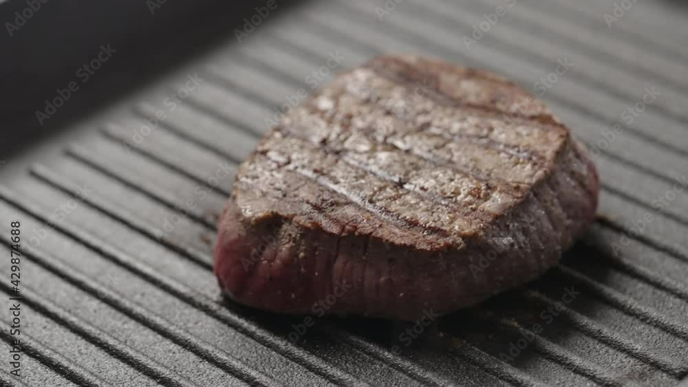 Slow motion handheld shot of beef steak cooking on iron grill pan Slow motion handheld shot of beef steak cooking on iron grill pan