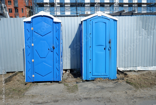 plastic mobile dry closets on a construction site for workers against the background of a metal temporary fence.