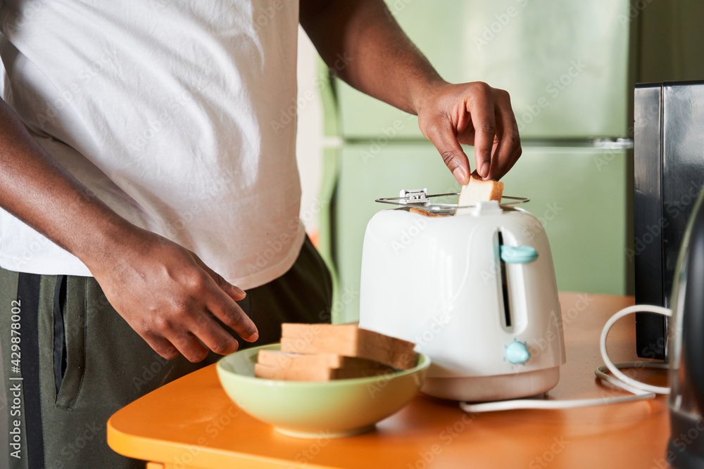 Man putting white toast bread to the toaster during the breakfast Man putting white toast bread to the toaster during the breakfast