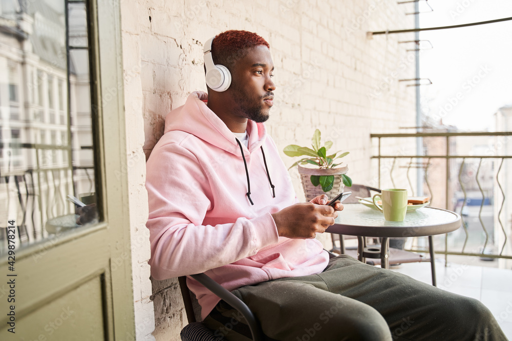 Fototapeta premium Man wearing headset listening music and looking away while sitting with smartphone at the hands
