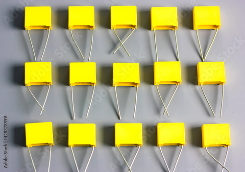 Yellow film capacitors isolated on gray background top view. Many square shape plastic electronic radio components on the gray surface with contrast shadows flatly. Selective focus. photo