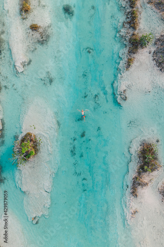People swimming in sunny seven colored lagoon surrounded by tropical plants in Bacalar, Quintana Roo, Mexico