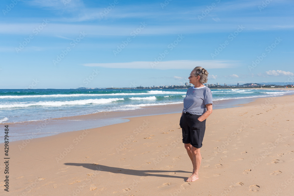 Full length view of senior woman looking at ocean (selective focus)
