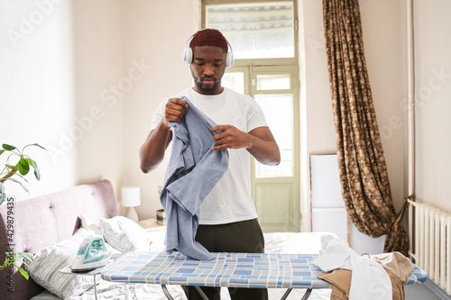 Man wearing headphones preparing to ironing clothes with pleasure smile photo