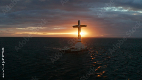 Catholic cross in sunken cemetery in the sea at sunset, aerial drone. colorful sky during the sunset. Large crucafix marking the underwater sunken cemetary, Camiguin Island Philippines.