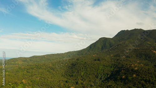 Mountains covered rainforest, trees and blue sky with clouds, aerial view. Camiguin, Philippines. Mountain landscape on tropical island with mountain peaks covered with forest. Slopes of mountains