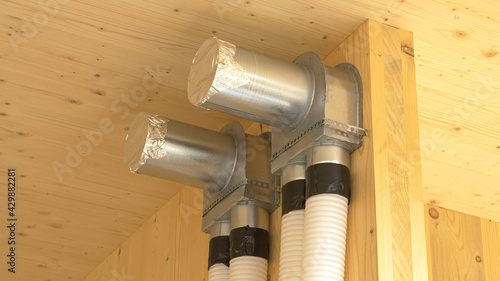 Foto CLOSE UP: Recuperation system exchanger and two tubes run down a hardwood wall