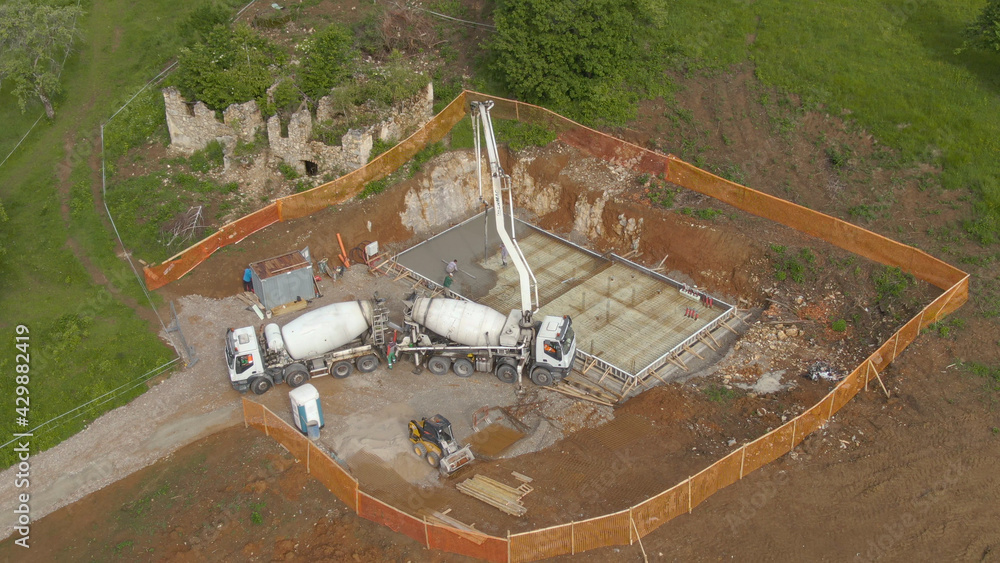 DRONE: Workers pouring concrete from a truck, creating the house foundation. DRONE: Workers pouring concrete from a truck, creating the house foundation.