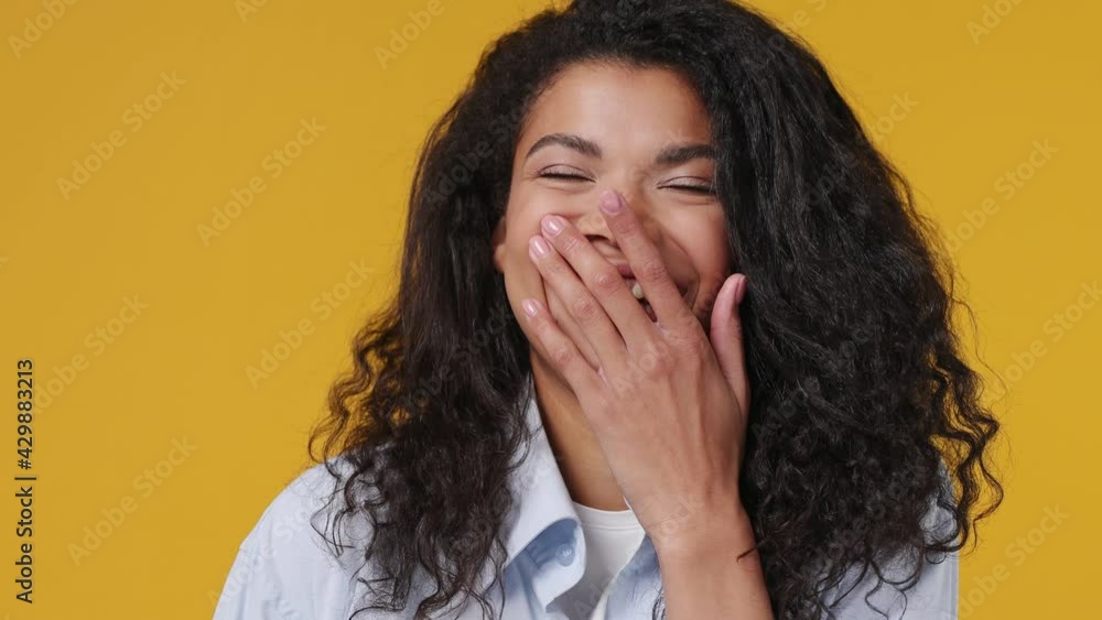 Close up young blithesome charismatic african woman curly hair 20s years old wears blue white t shirt smiling laugh isolated on yellow color wall background studio. People emotions lifestyle concept Close up young blithesome charismatic african woman curly hair 20s years old wears blue white t shirt smiling laugh isolated on yellow color wall background studio. People emotions lifestyle concept