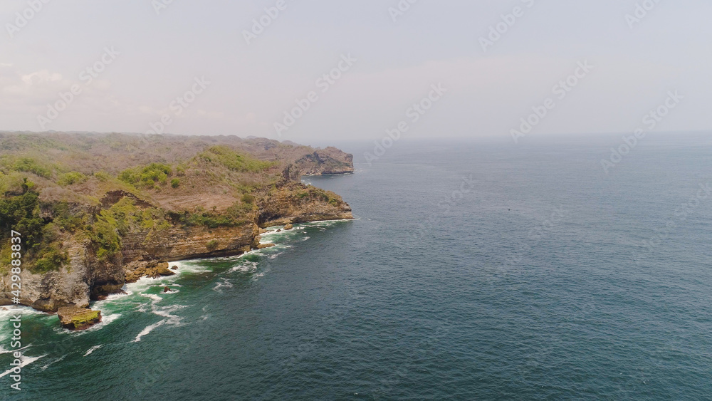 aerial view rocky coastline with cliffs, ocean surf with breaking waves in coast. seascape waves break on rocky shore java, indonesia