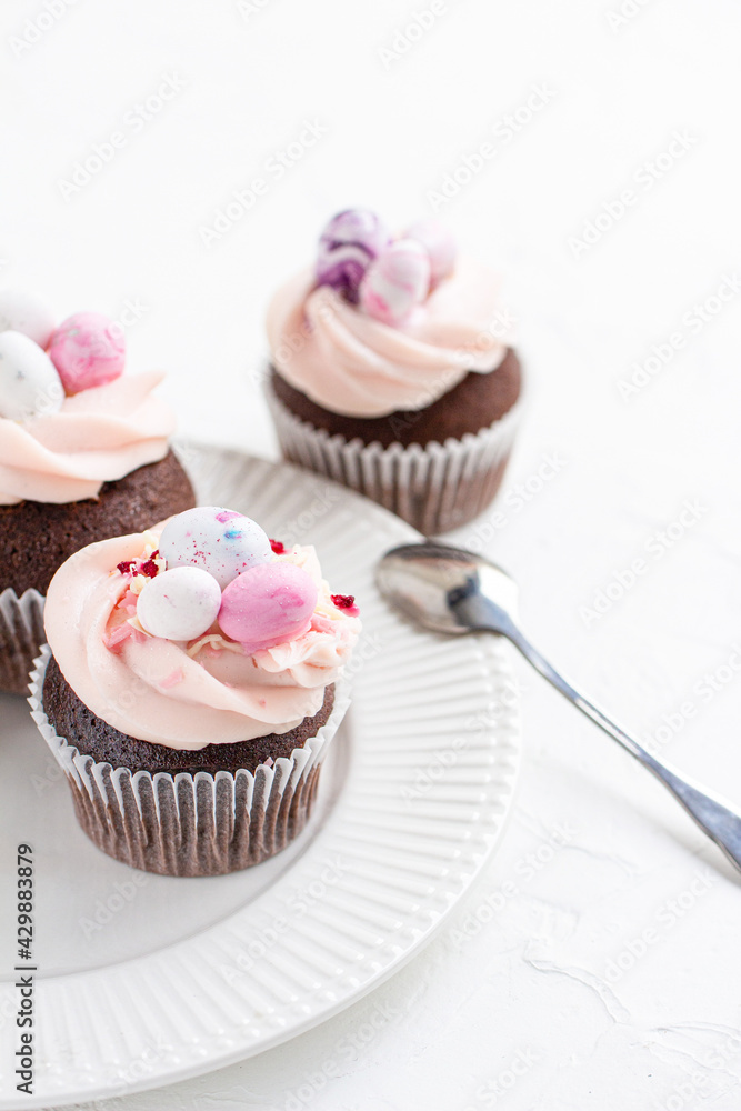 Three Easter chocolate cupcakes with caramel filling and decoration of small Easter eggs from marzipan on a white porcelain plate. Selective focus