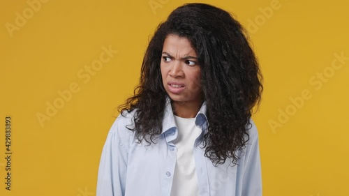 Young african woman curly hair 20s years old wear blue white t shirt look aside around one guy nice other disapprovingly different emotions like dislike isolated on yellow color wall background studio photo