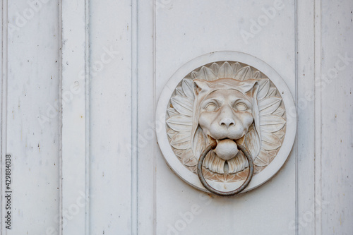 Detail of white antique tiger or lion bas relief sculpture and metal door knocker's ring on wooden white door. photo