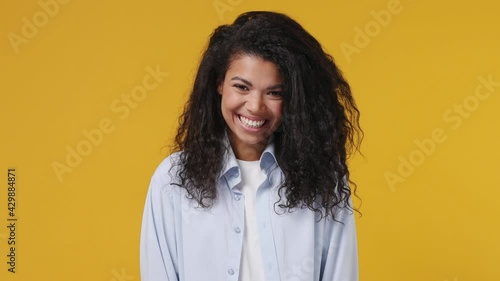 Young african woman wears blue white t shirt pointing index fingers on blow puffing cheeks with funny face mouth inflated with air crazy expression squint eyes isolated on yellow color wall background photo