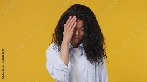 Sad upset ashamed tired young african woman curly hair 20s years old wears blue white t shirt put hand on face facepalm epic fail mistaken omg gesture isolated on yellow color wall background studio photo