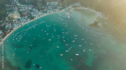 Aerial drone town on the coast with bay and lot tourist boats at sunrise, El nido, Palawan, Philippines. Seascape with blue bay and boats view from above. Summer and travel vacation concept