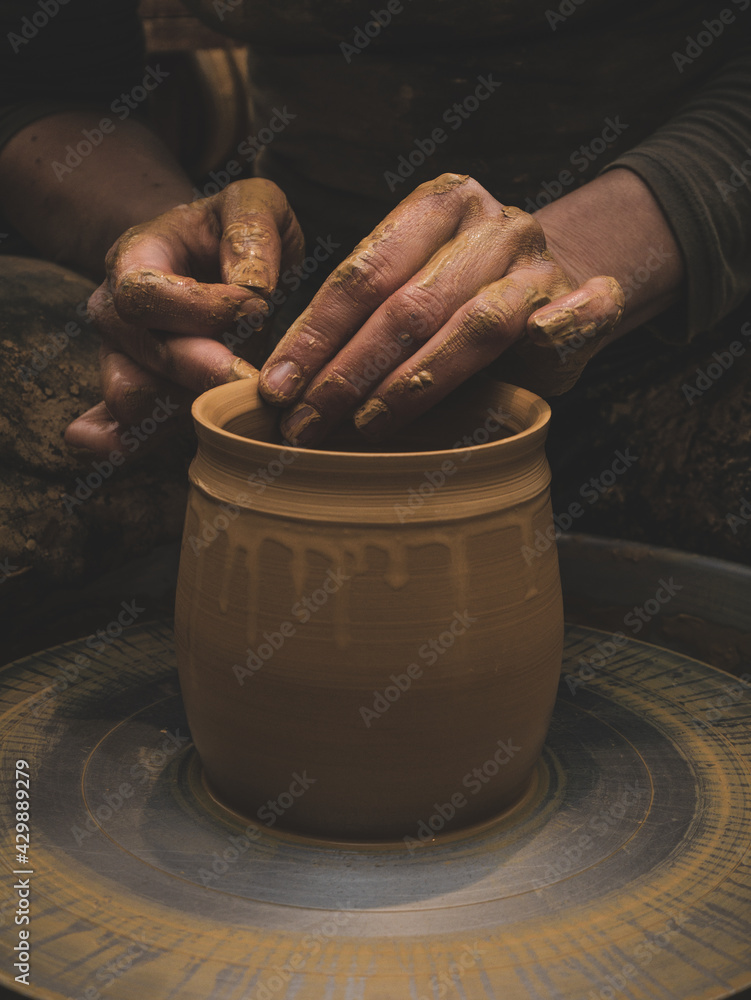 Vertical photo of hands making a pot with clay.