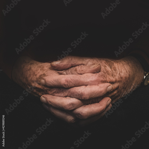 Intertwined hands of an elderly woman in the middle of a black background.