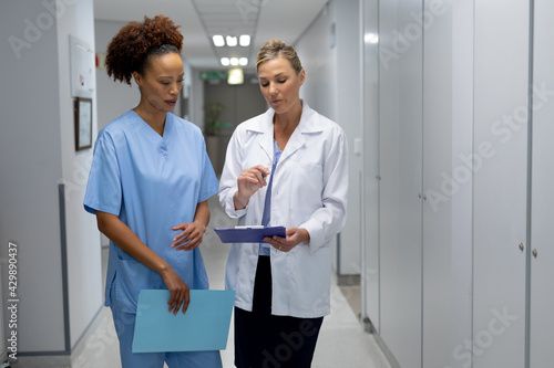 Two diverse female doctors standing in hospital corridor looking at medical chart document