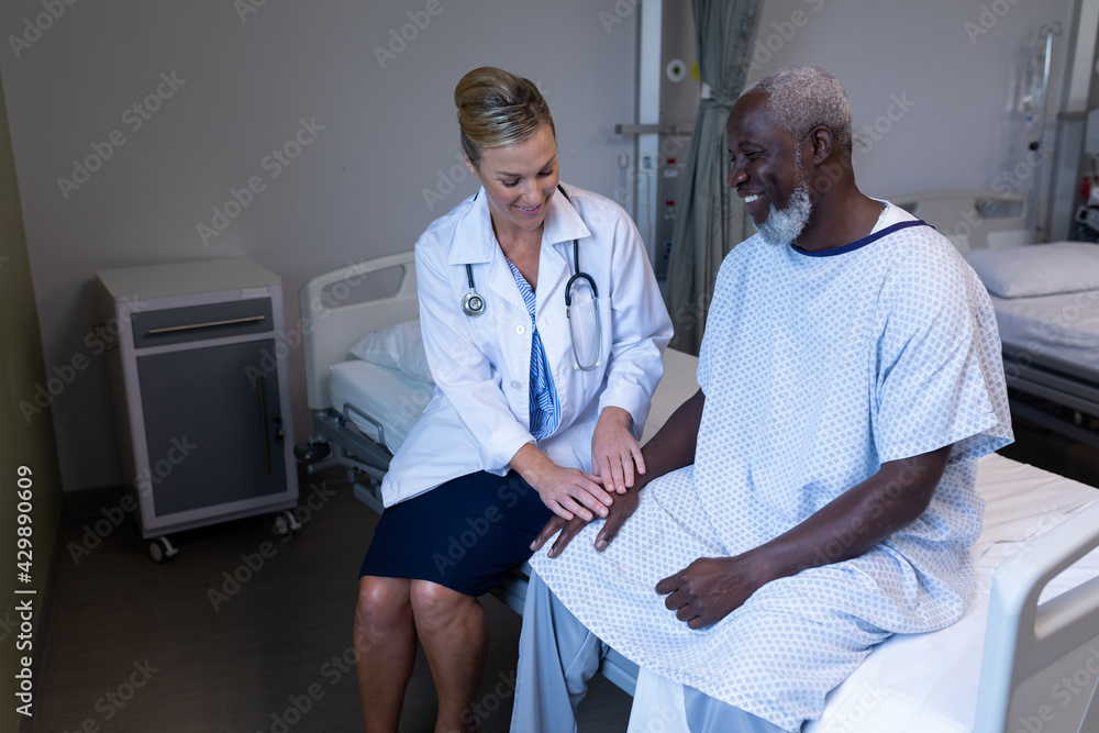Caucasian female doctor sitting on hospital bed touching hand of african american male and smiling Caucasian female doctor sitting on hospital bed touching hand of african american male and smiling