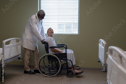 Diverse male doctor and female patient sitting on wheelchair smiling to each other