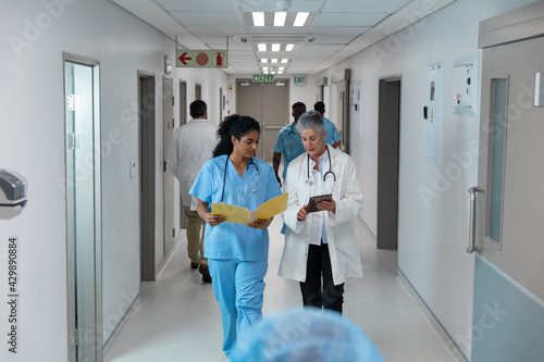 Diverse male and female doctors walking through hospital corridor discussing