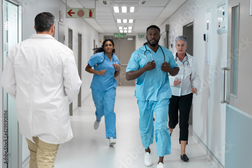Diverse group of male and female doctors running through busy hospital corridor