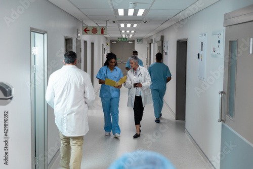 Diverse male and female doctors walking through hospital corridor discussing