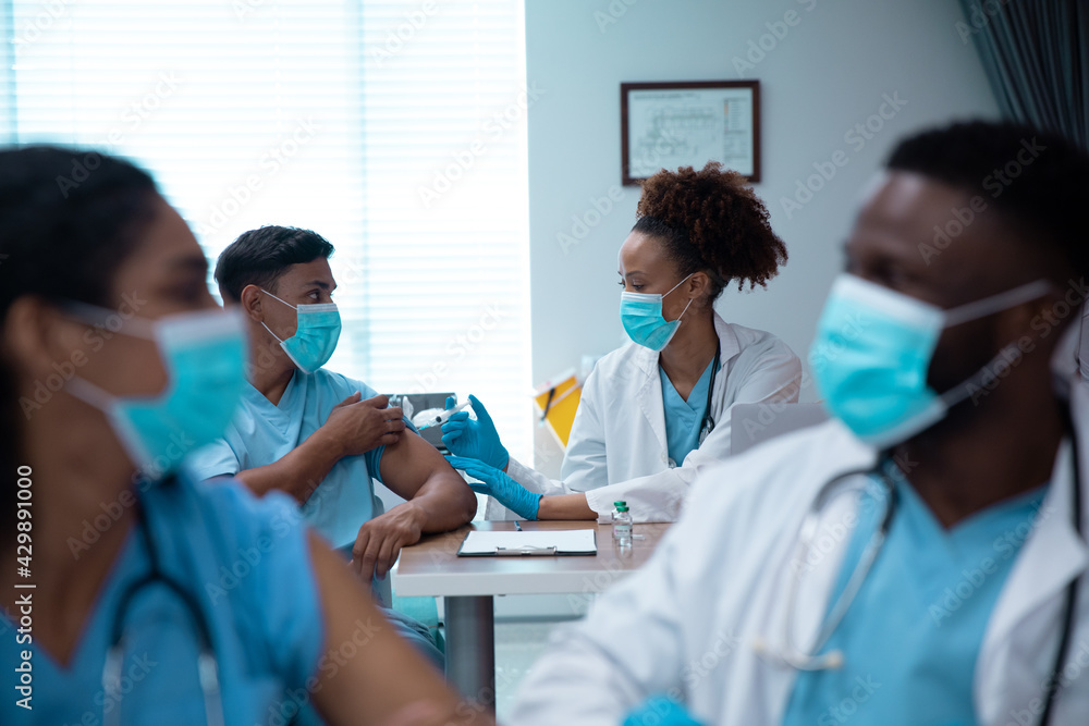 Mixed race couple of doctors wearing face masks making injection Mixed race couple of doctors wearing face masks making injection