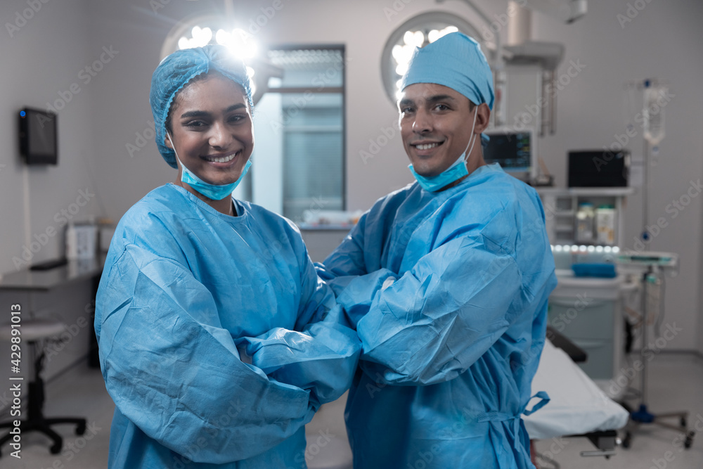 Smiling diverse male female surgeons with face masks and protective clothing in operating theatre Smiling diverse male female surgeons with face masks and protective clothing in operating theatre