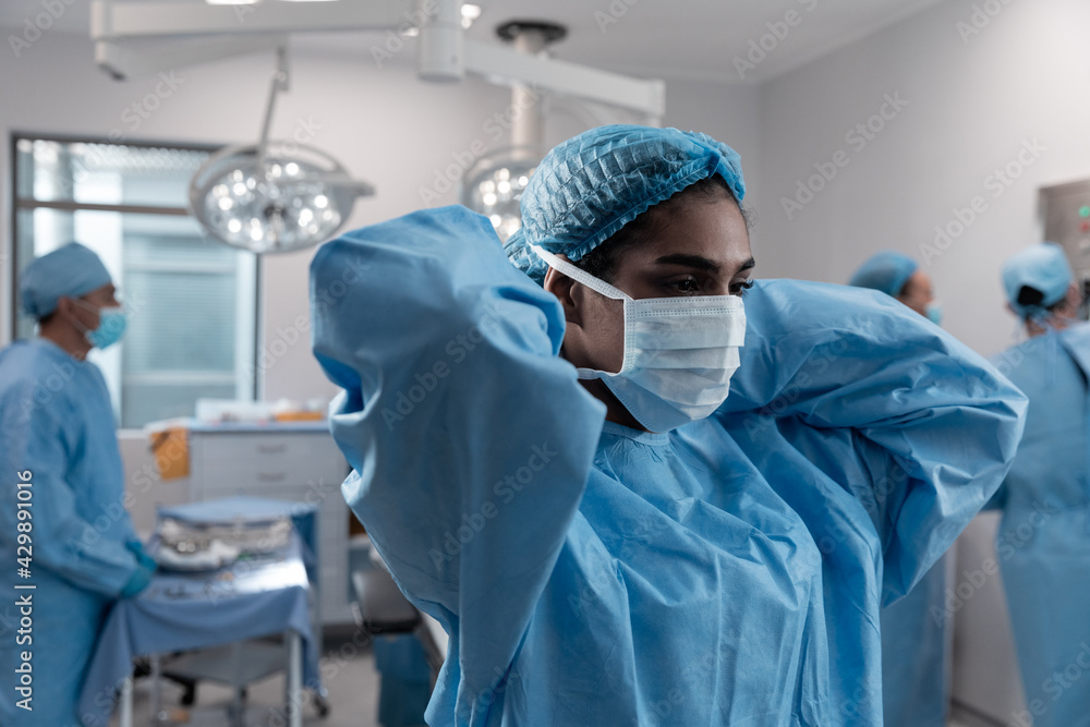 Mixed race female doctor putting on face mask standing in operating theatre Mixed race female doctor putting on face mask standing in operating theatre