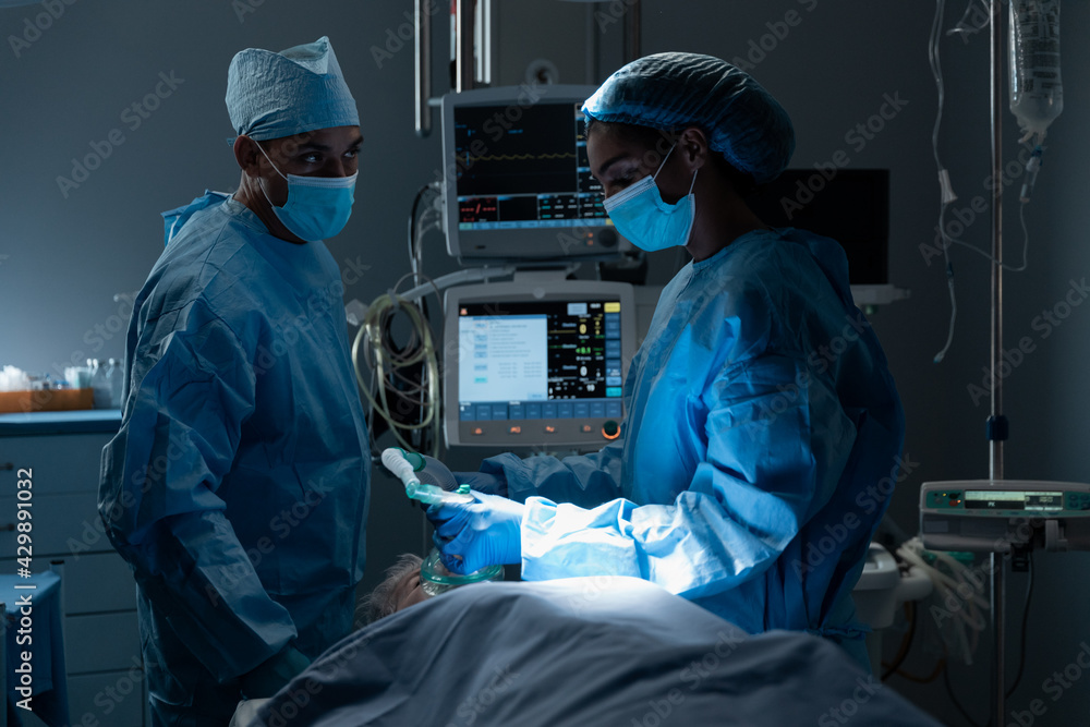Diverse surgeons with face masks and protective clothing during operation, sedating patient Diverse surgeons with face masks and protective clothing during operation, sedating patient