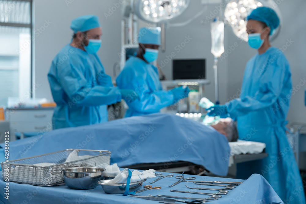Diverse male and female doctors wearing face masks and surgical overalls in operating theatre Diverse male and female doctors wearing face masks and surgical overalls in operating theatre