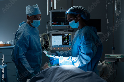 Diverse surgeons with face masks and protective clothing during operation, sedating patient