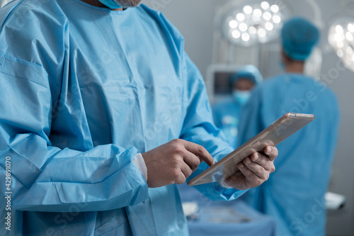 Midsection of caucasian male surgeon wearing protective clothing using tablet in operating theatre photo
